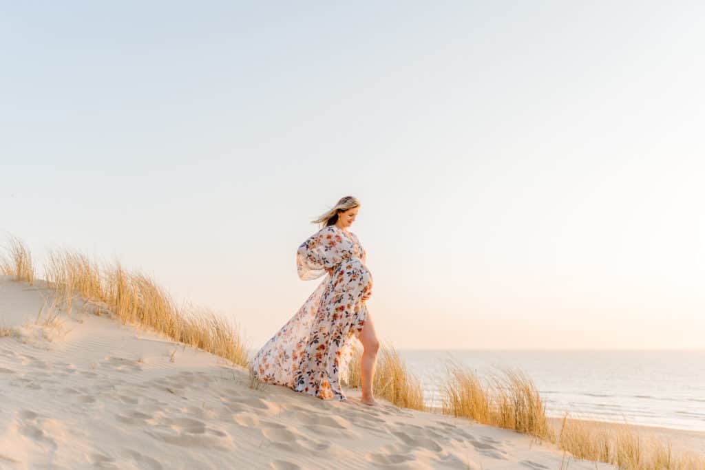 An expectant mother stands on a sandy beach, with waves crashing behind her, captured in a beautiful maternity photo.